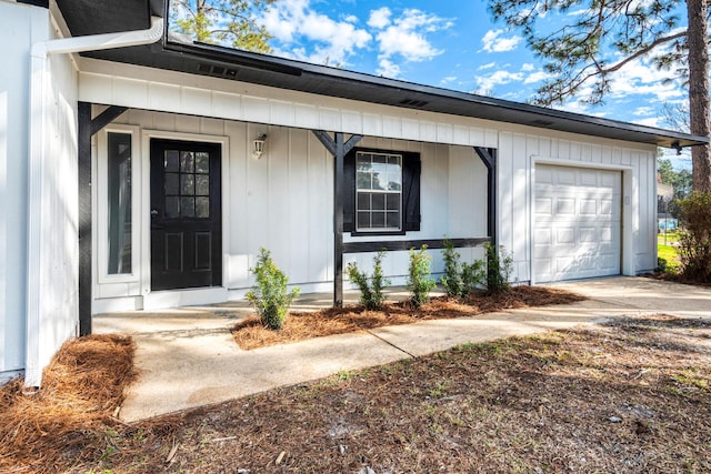 doorway to property featuring an attached garage, a porch, board and batten siding, and concrete driveway