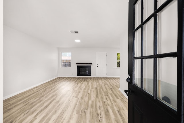 unfurnished living room with light wood-type flooring, a glass covered fireplace, a healthy amount of sunlight, and visible vents