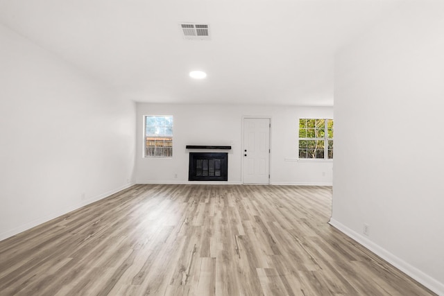 unfurnished living room with baseboards, a glass covered fireplace, visible vents, and light wood-style floors