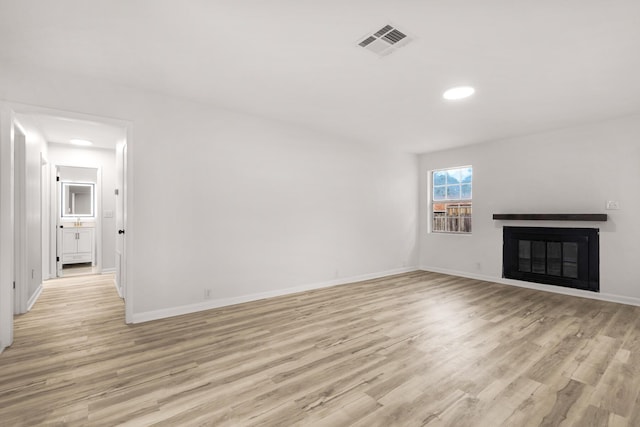 unfurnished living room with light wood-style floors, a glass covered fireplace, visible vents, and baseboards