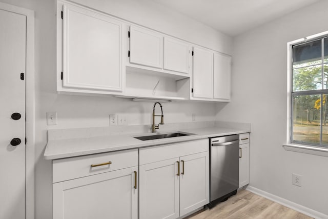 kitchen with light countertops, light wood-style flooring, stainless steel dishwasher, white cabinetry, and a sink