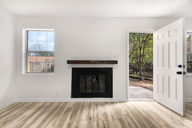 unfurnished living room with a glass covered fireplace, baseboards, and wood finished floors