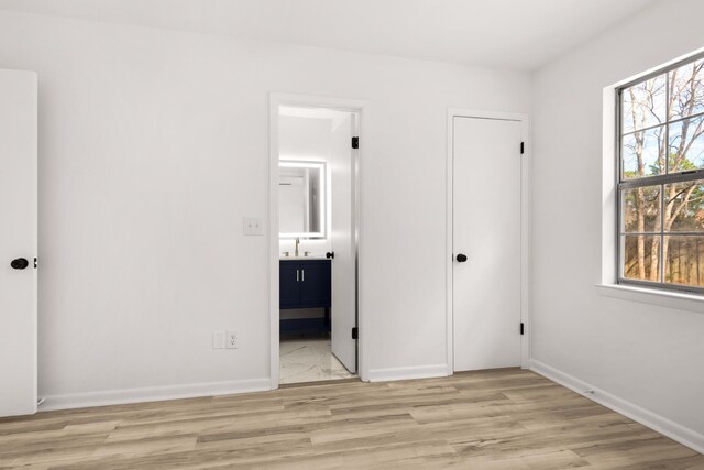 unfurnished bedroom featuring light wood-style floors, baseboards, a sink, and ensuite bathroom