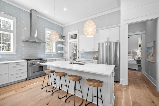 kitchen featuring high end appliances, a breakfast bar area, light wood-type flooring, wall chimney range hood, and a sink