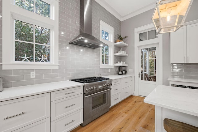 kitchen featuring wall chimney exhaust hood, decorative backsplash, stainless steel stove, and white cabinetry