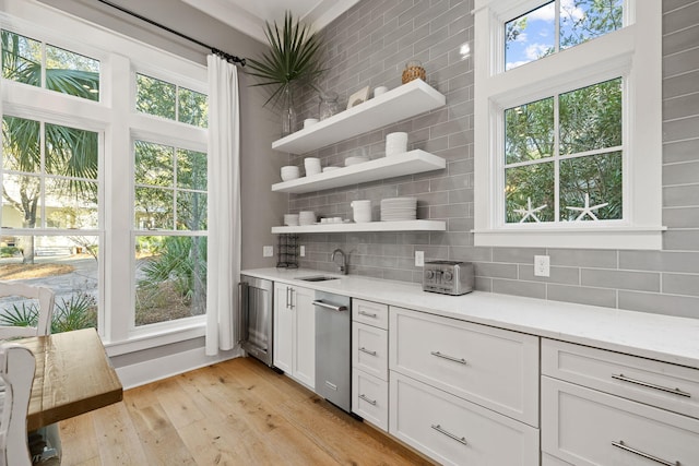 kitchen featuring tasteful backsplash, light countertops, light wood-style floors, white cabinets, and a sink