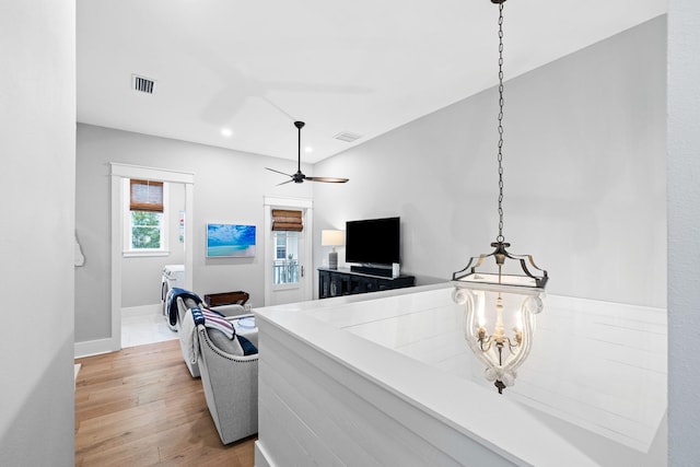 interior space with light wood-style flooring, visible vents, baseboards, and ceiling fan with notable chandelier