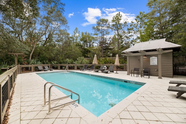 pool featuring a patio area, fence, and an outdoor structure