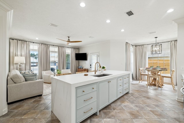 kitchen with light countertops, ornamental molding, open floor plan, a kitchen island with sink, and a sink