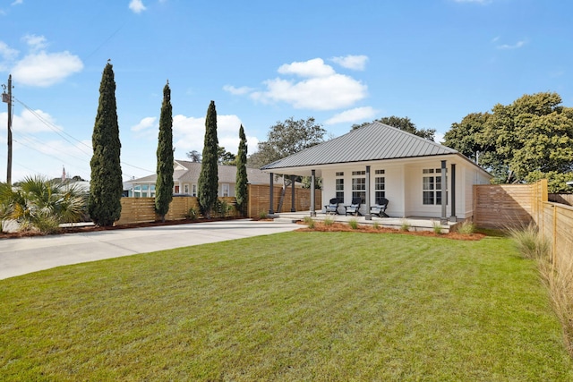 view of front of house with a patio, concrete driveway, a front yard, metal roof, and fence