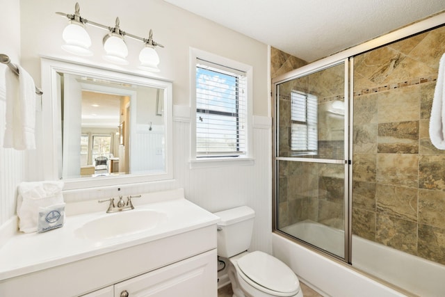 bathroom featuring wainscoting, toilet, vanity, and shower / bath combination with glass door