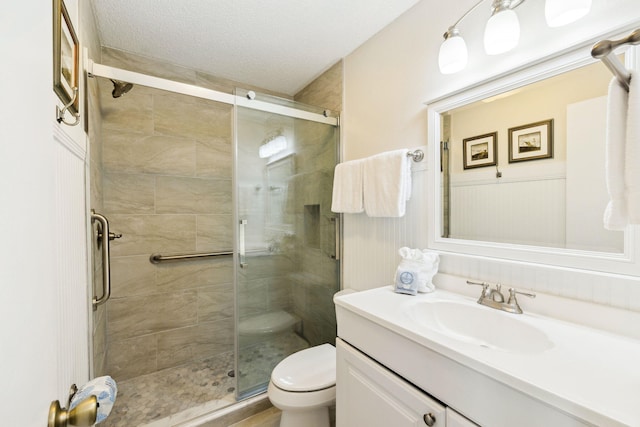 full bathroom featuring a shower stall, a wainscoted wall, toilet, vanity, and a textured ceiling