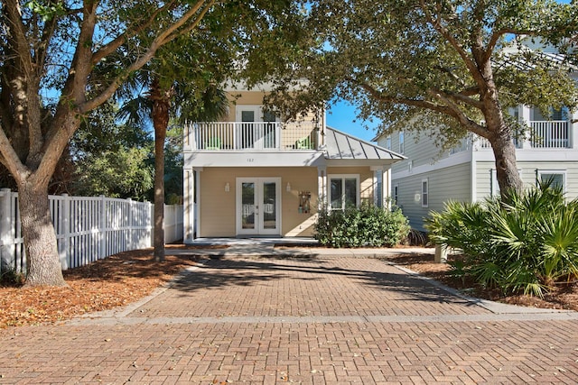 view of front of property featuring french doors, a standing seam roof, fence, a balcony, and metal roof