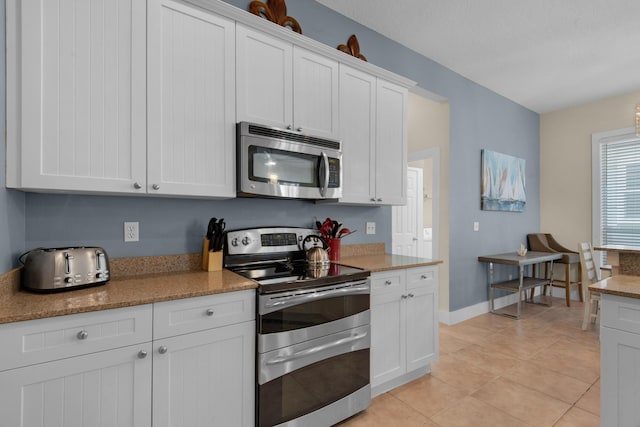 kitchen with light tile patterned floors, appliances with stainless steel finishes, baseboards, and white cabinets