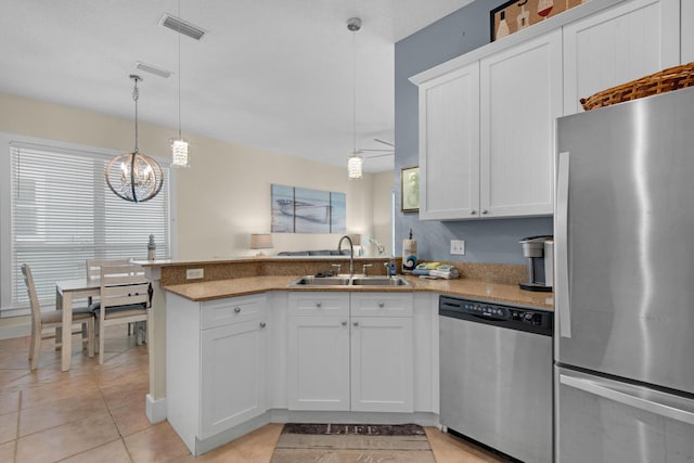 kitchen featuring light tile patterned floors, stainless steel appliances, white cabinetry, a sink, and a peninsula