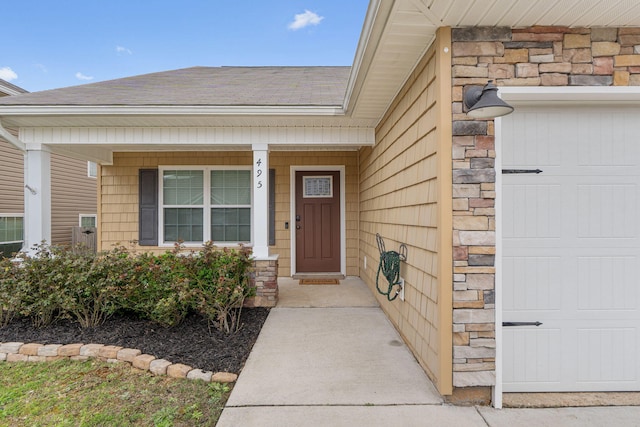 property entrance featuring a garage, stone siding, roof with shingles, and covered porch