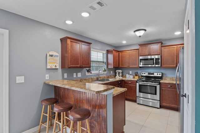 kitchen featuring visible vents, appliances with stainless steel finishes, a sink, a peninsula, and a kitchen bar