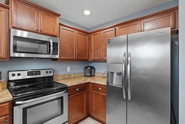 kitchen featuring a textured ceiling, appliances with stainless steel finishes, and brown cabinetry