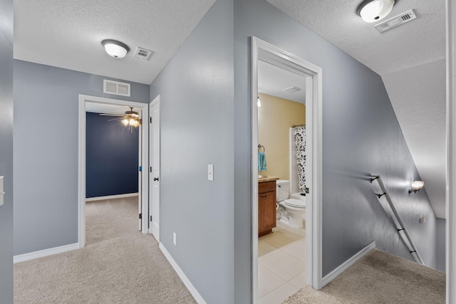 hallway featuring visible vents, a textured ceiling, light carpet, and an upstairs landing