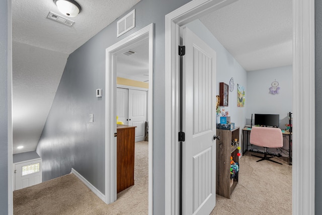 hallway featuring light colored carpet, visible vents, and a textured ceiling