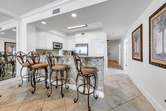 kitchen featuring visible vents, a breakfast bar area, a peninsula, stainless steel appliances, and white cabinetry