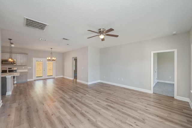 unfurnished living room featuring ceiling fan with notable chandelier, baseboards, visible vents, and light wood-style floors