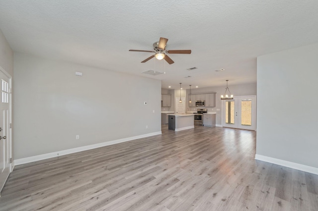 unfurnished living room with ceiling fan with notable chandelier, light wood-style flooring, baseboards, and a textured ceiling