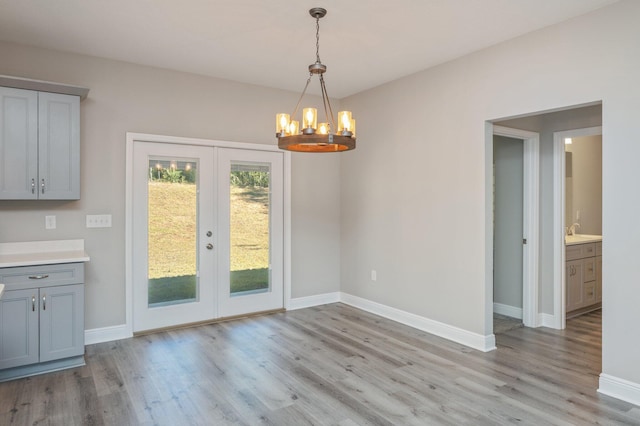 unfurnished dining area featuring french doors, light wood-type flooring, a sink, and baseboards