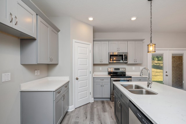 kitchen featuring stainless steel appliances, gray cabinetry, light wood-style floors, pendant lighting, and a sink