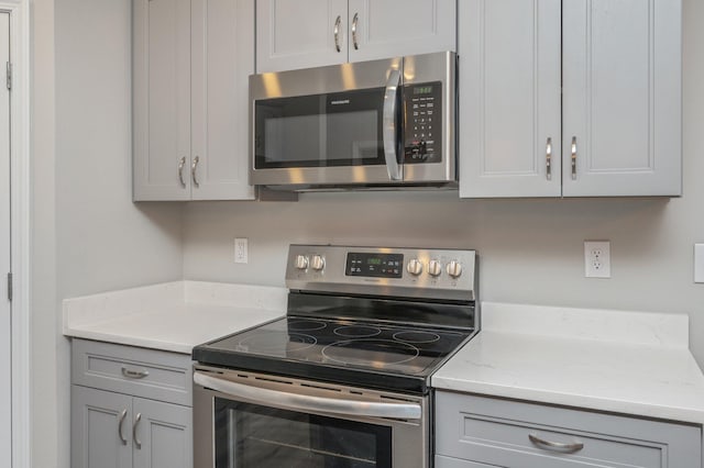 kitchen with stainless steel appliances, light stone countertops, and gray cabinetry