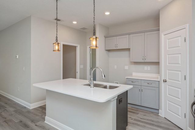 kitchen featuring visible vents, light wood-style flooring, hanging light fixtures, gray cabinets, and a sink