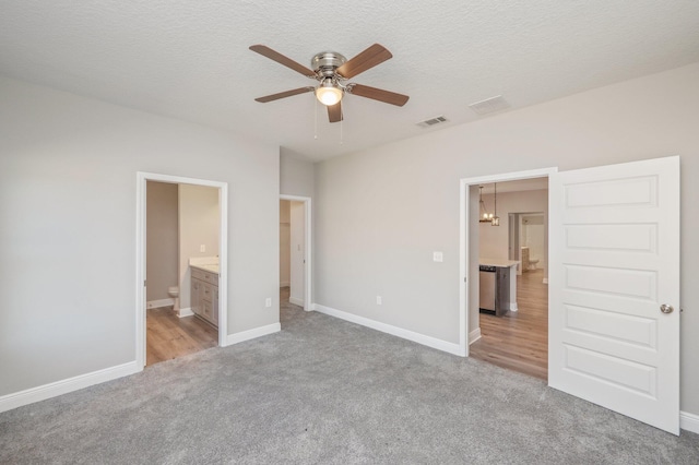 unfurnished bedroom featuring light colored carpet, visible vents, a textured ceiling, and ensuite bath