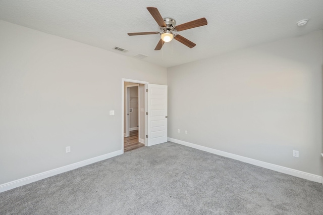 empty room featuring carpet, visible vents, a ceiling fan, a textured ceiling, and baseboards