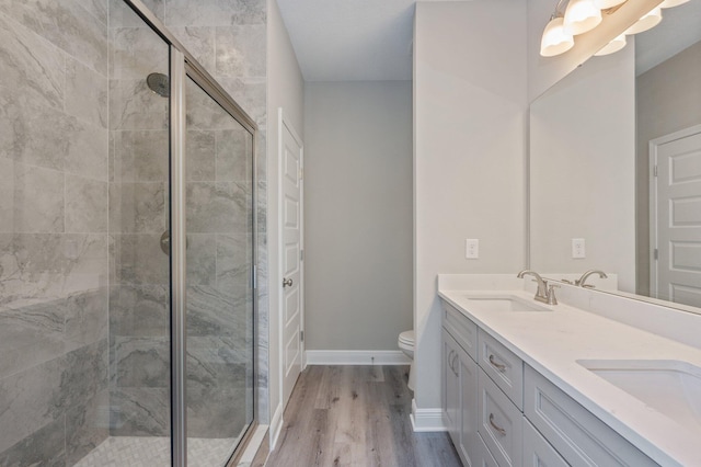 bathroom featuring double vanity, a stall shower, a sink, wood finished floors, and baseboards