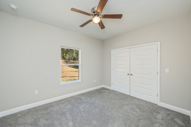 unfurnished bedroom with ceiling fan, a closet, dark carpet, and baseboards