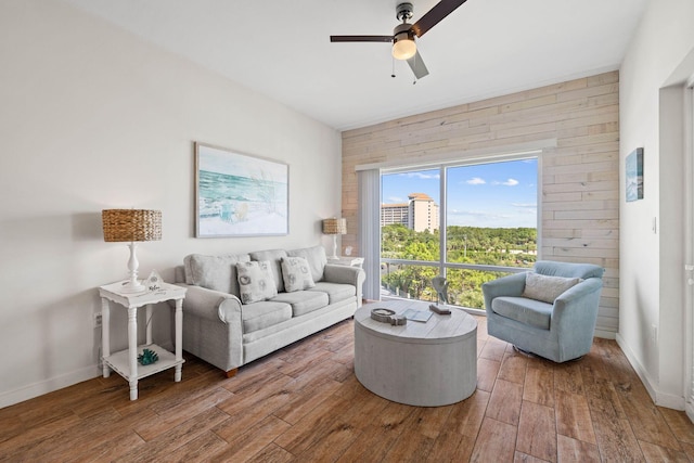 living room with ceiling fan, wooden walls, wood finished floors, and baseboards