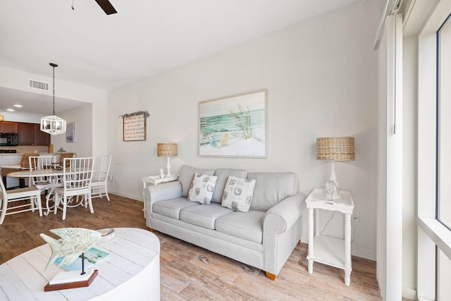 living room featuring light wood-style flooring, visible vents, ceiling fan, and baseboards