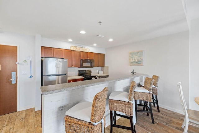 kitchen with black appliances, brown cabinetry, light countertops, and light wood-style flooring