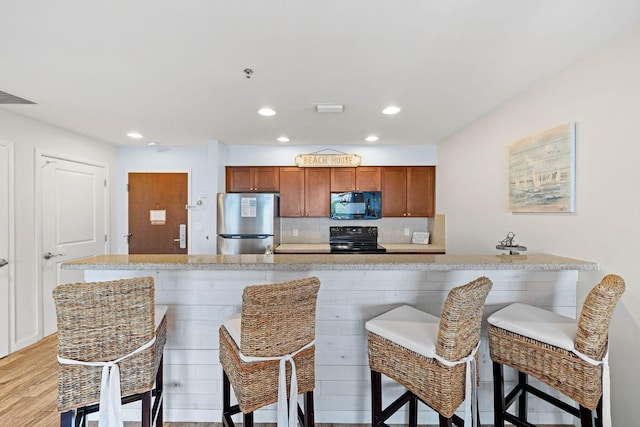 kitchen featuring tasteful backsplash, light wood-style floors, light countertops, black appliances, and a kitchen bar