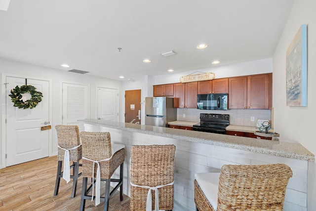 kitchen with light wood finished floors, a breakfast bar area, black appliances, backsplash, and recessed lighting