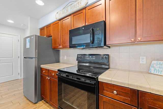 kitchen with tile countertops, light wood-type flooring, decorative backsplash, brown cabinets, and black appliances