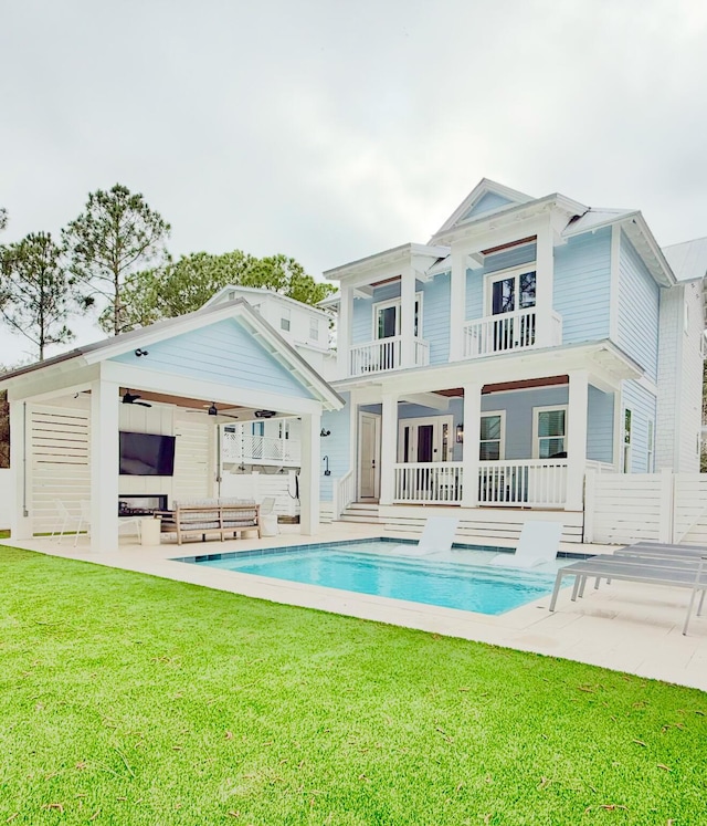 back of house featuring a patio, a balcony, a ceiling fan, an outdoor pool, and a lawn