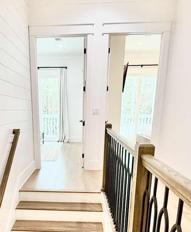 hallway featuring wood finished floors, an upstairs landing, visible vents, and wood walls