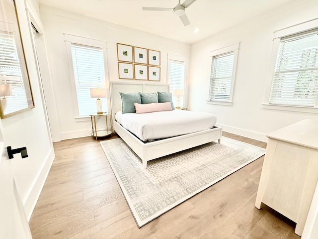 bedroom with a ceiling fan, multiple windows, light wood-style floors, and baseboards