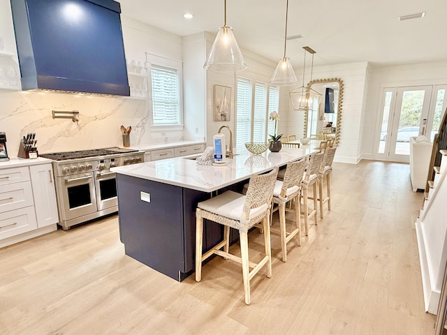 kitchen featuring a kitchen bar, double oven range, backsplash, light wood-style floors, and exhaust hood