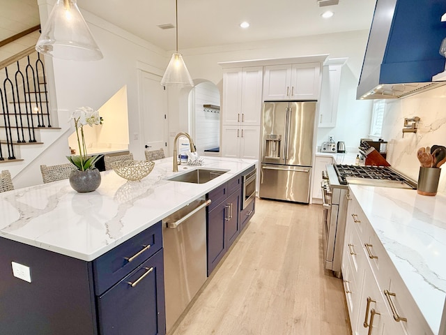 kitchen with a sink, blue cabinetry, white cabinetry, wall chimney exhaust hood, and high end appliances