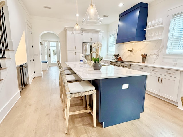 kitchen featuring light wood finished floors, tasteful backsplash, premium range hood, arched walkways, and stove