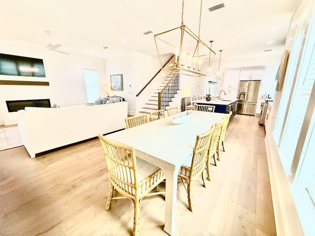 dining space with a glass covered fireplace, stairway, light wood-style flooring, and visible vents