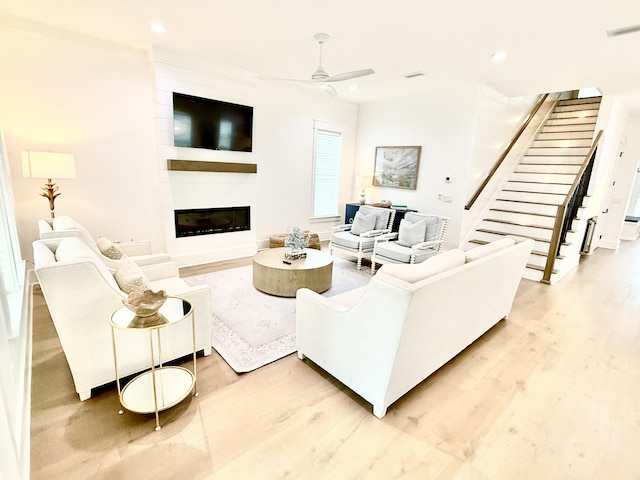 living room featuring light wood finished floors, a large fireplace, stairs, recessed lighting, and a ceiling fan