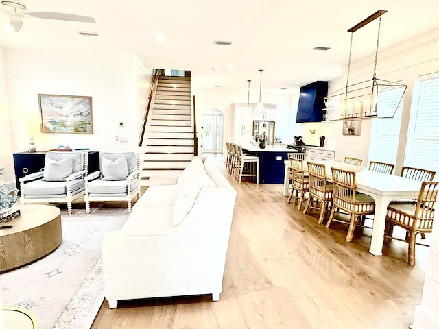 living room featuring visible vents, arched walkways, light wood-style flooring, and stairs